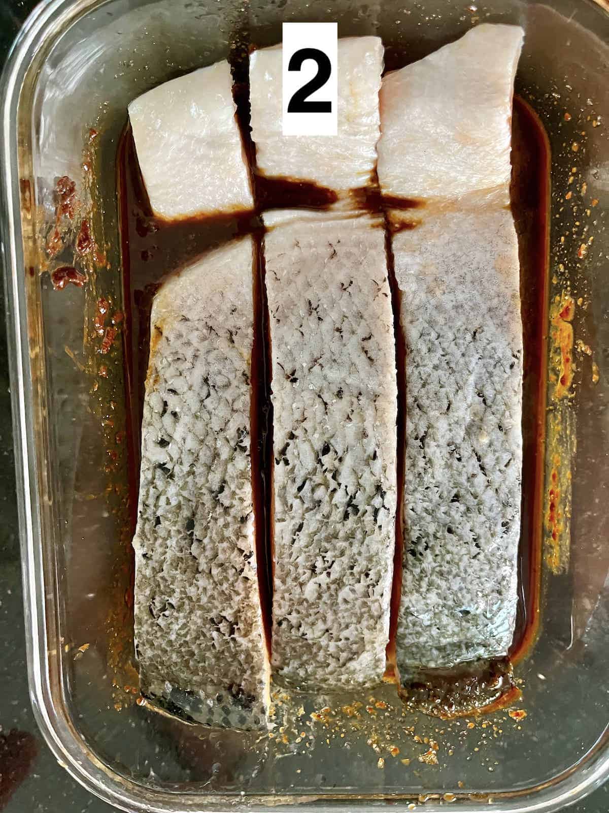 Salmon fillets flesh down in a marinade, skin facing up.