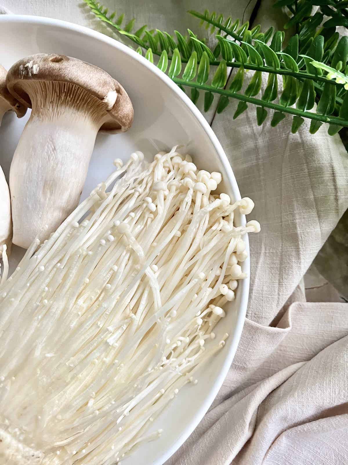 Close-up of long enoki mushrooms next to eryngii mushrooms.