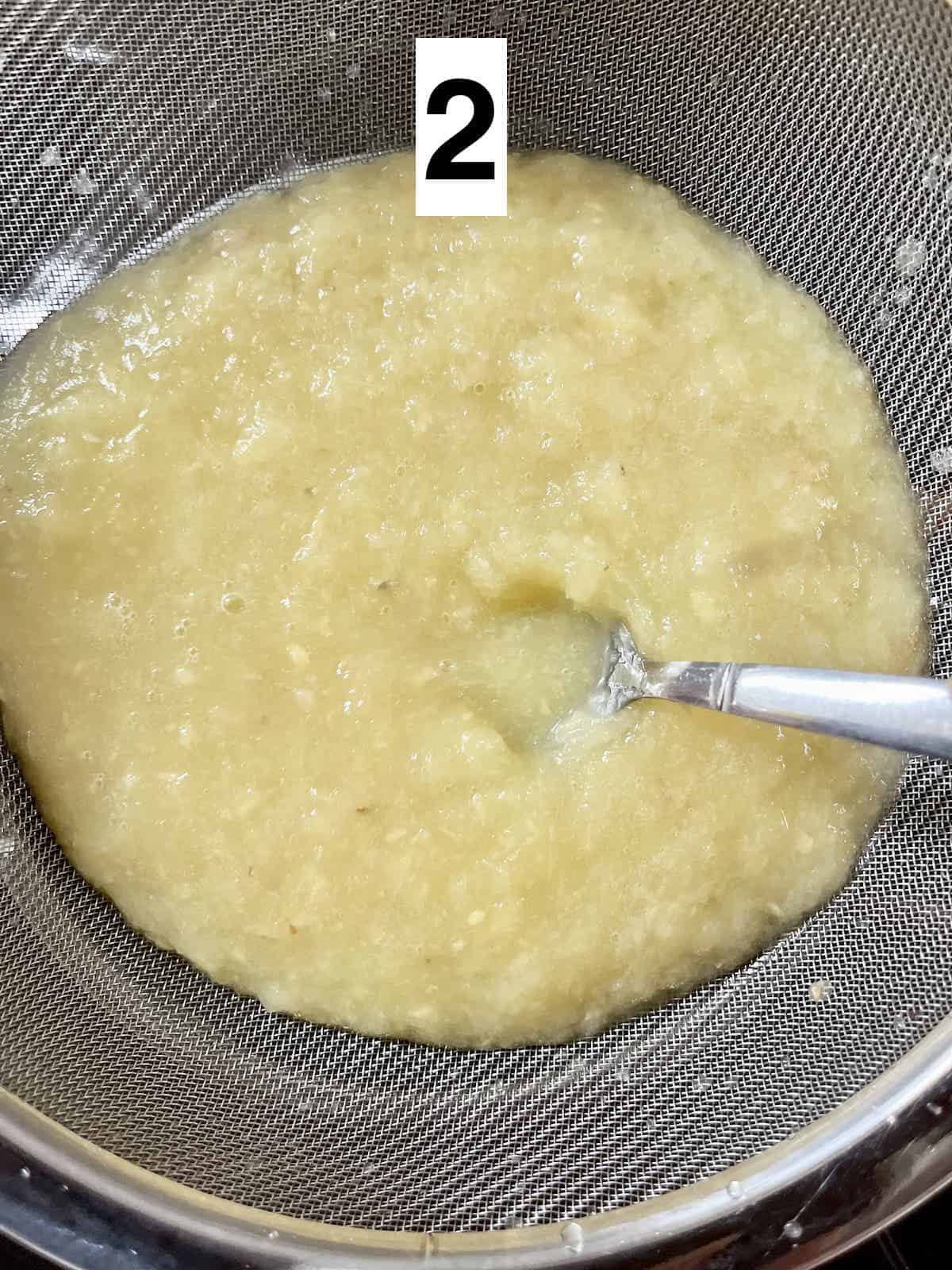 Straining blended pineapple and ginger through a metal sieve.