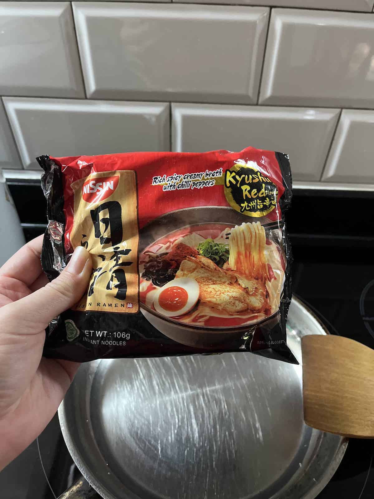 A packet of Instant ramen over a pan of water.