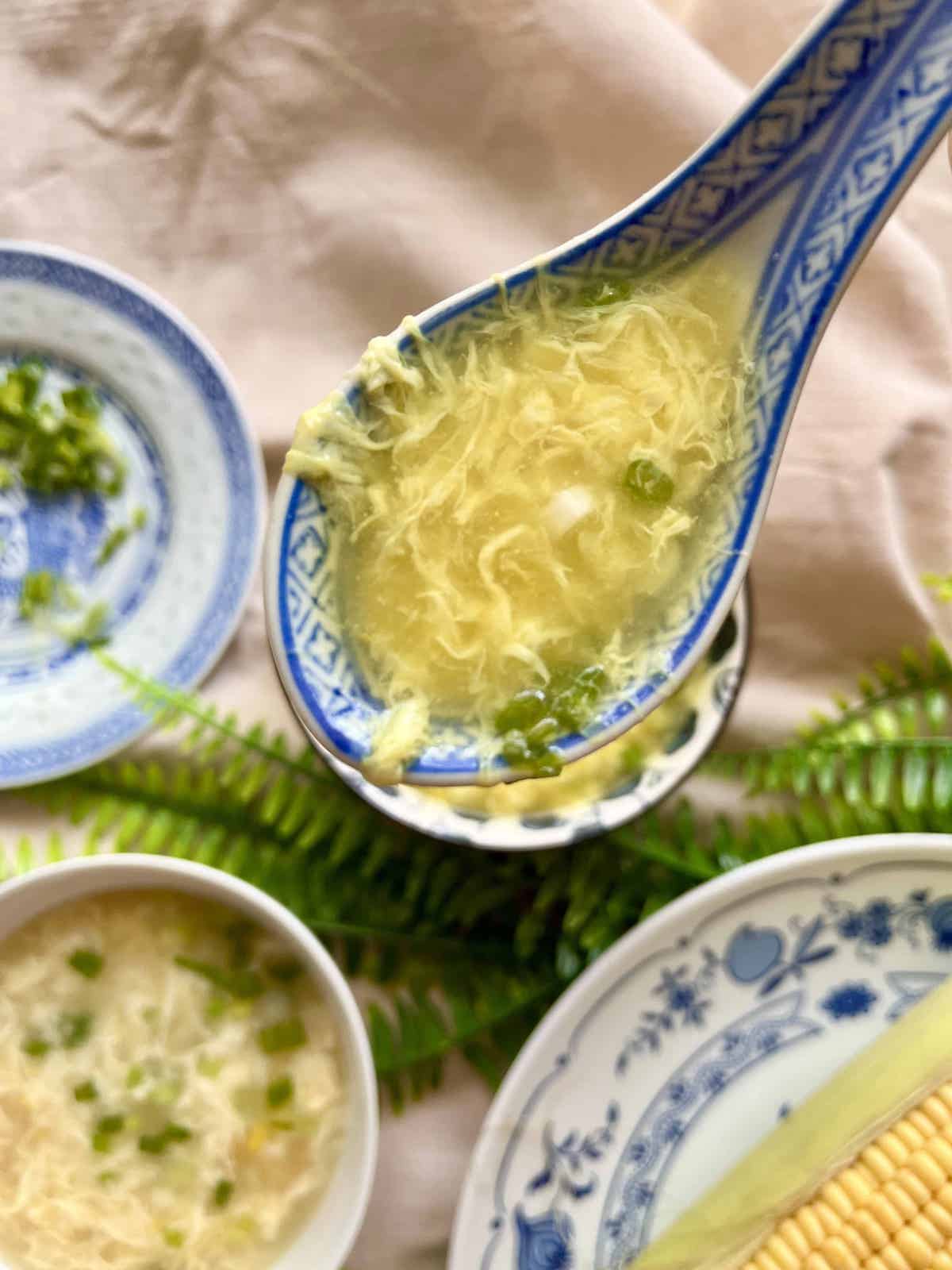 A spoonful off corn soup with egg ribbons and spring onions.