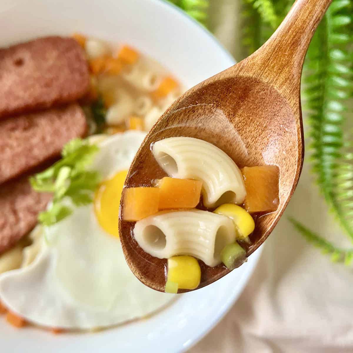 Close-up of a spoonful of Macaroni Soup with carrots, corn and SPAM.