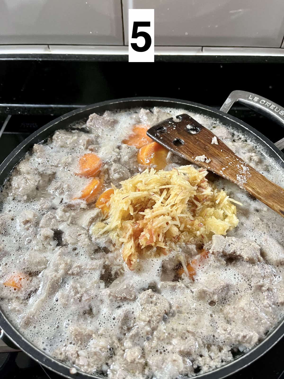 Adding grated apple to the simmering pork and carrots.