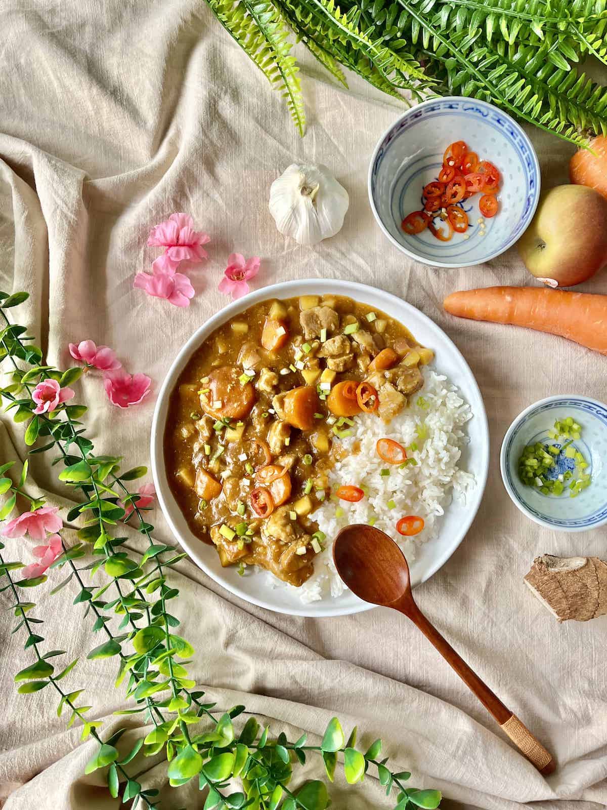 Japanese curry, with pork, carrots and green onions, next to white rice on a white plate.