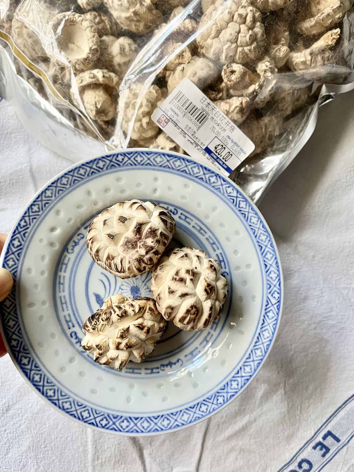 3 dried shiitake mushrooms on a plate next to a bag of them.