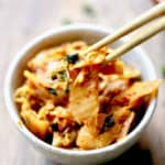 A close-up of kimchi being picked out of a bowl with a pair of chopsticks