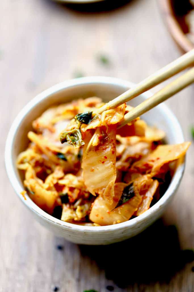 A close-up of kimchi being picked out of a bowl with a pair of chopsticks