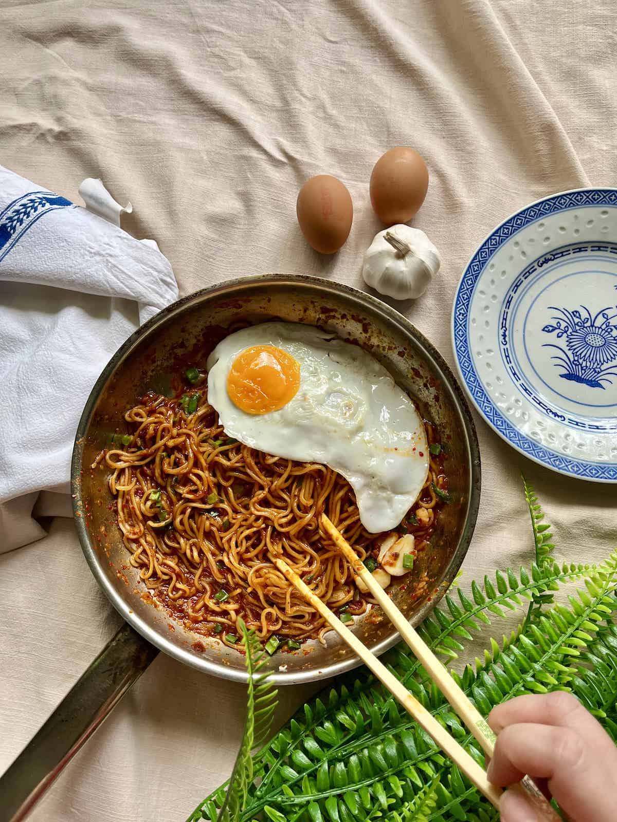 Someone taking noodles from a pan of Gochujang Noodles with a fried egg on top.