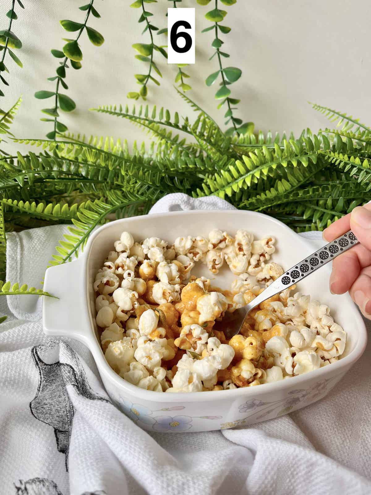 Pouring salted egg yolk sauce onto popcorn and mixing it.