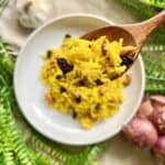 Close-up of turmeric rice with raisins on a wooden spoon.