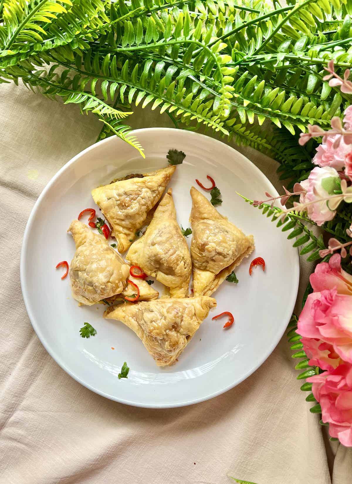 5 baked samosas on a plate with ed rchilies and coriander.