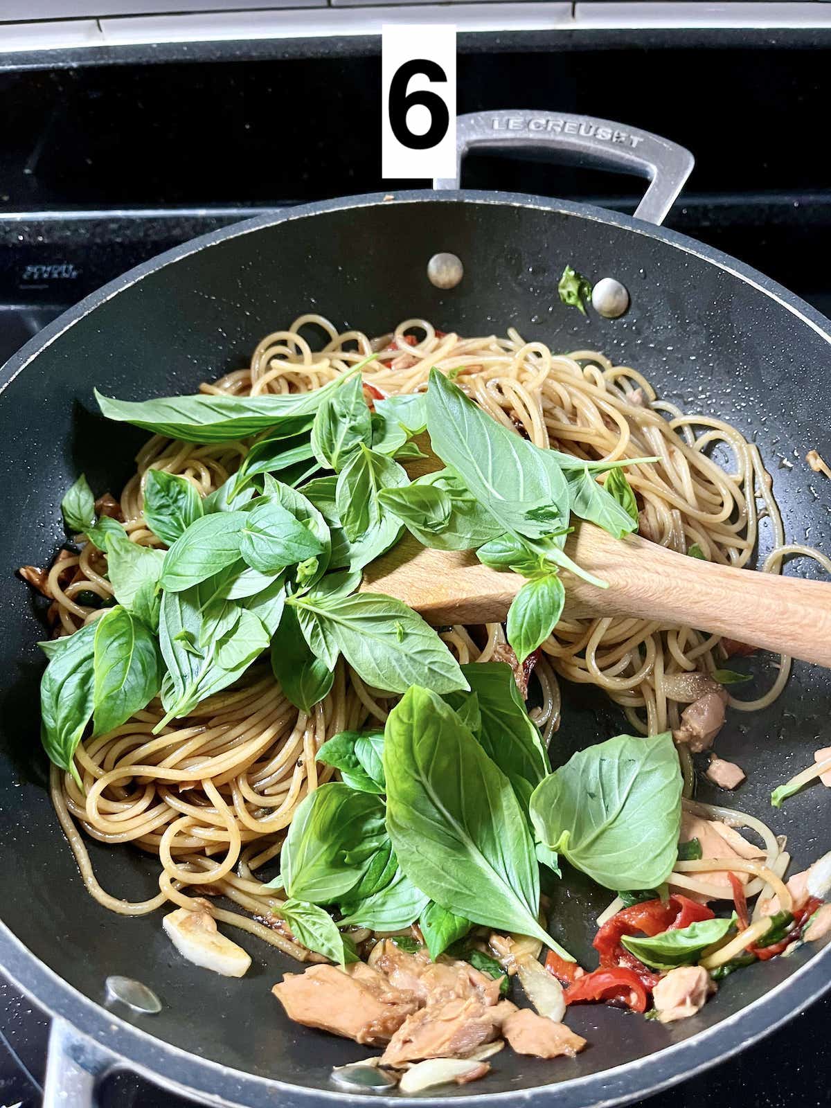 Adding Thai basil leaves to a spicy spaghetti.