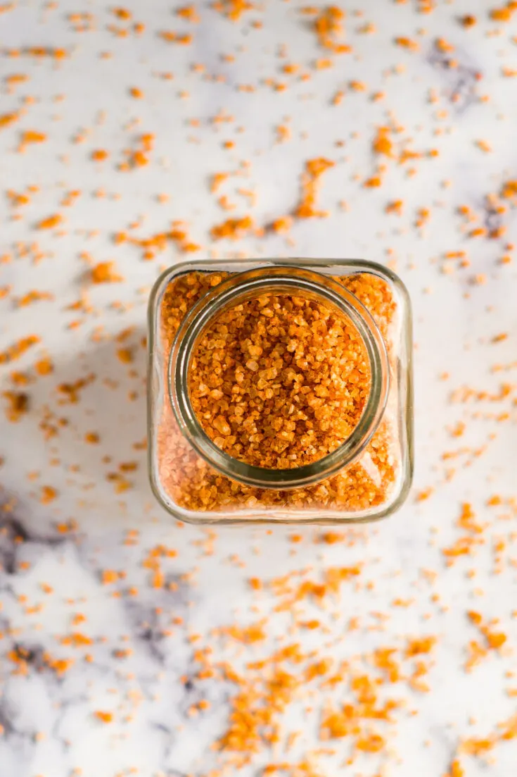 A glass jar full of sriracha salt with some sprinkled around it