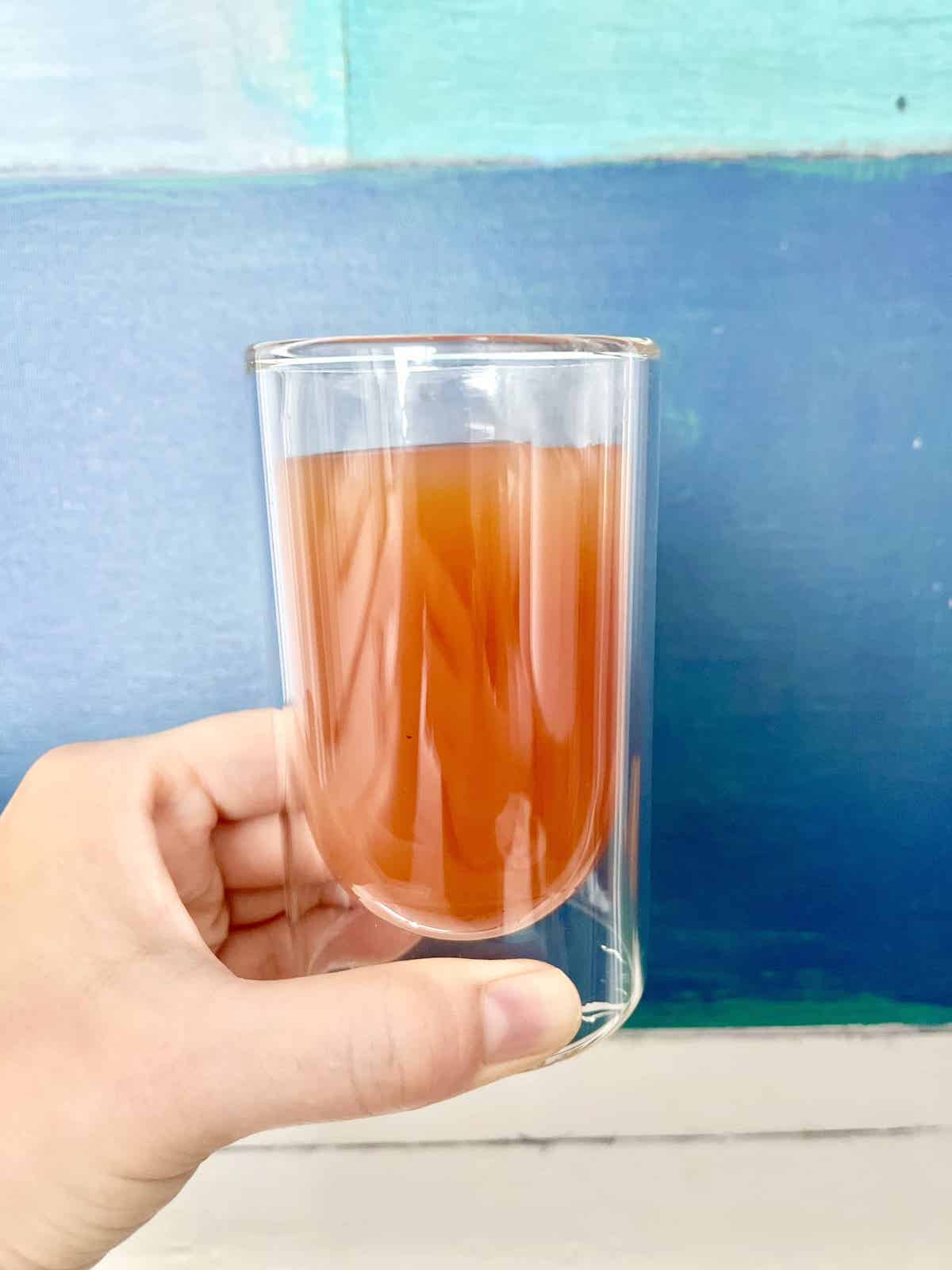 A cup of homemade Starbucks copycat guava black tea held against a blue backdrop.