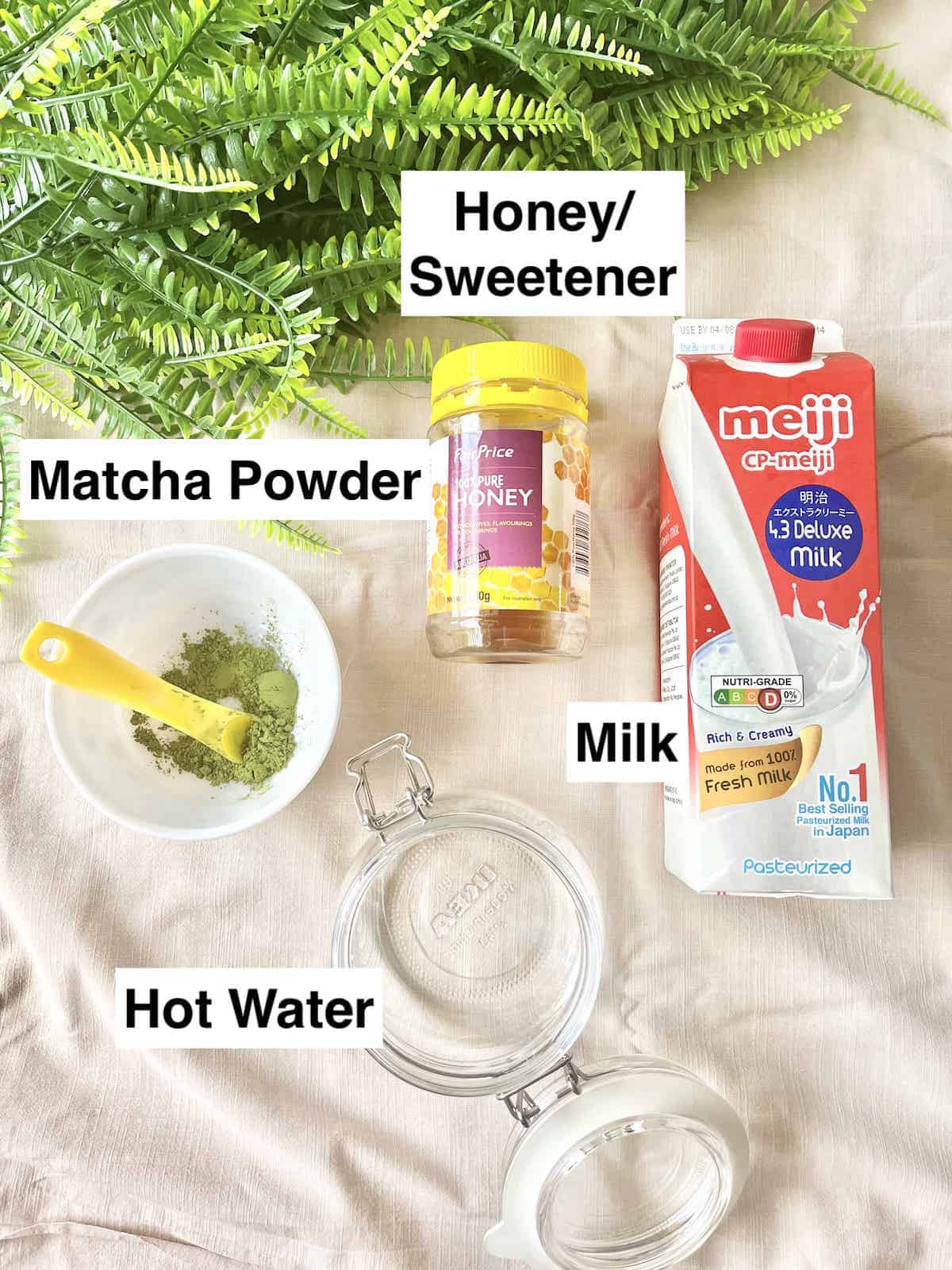 Matcha powder, water, honey and milk next to each other.