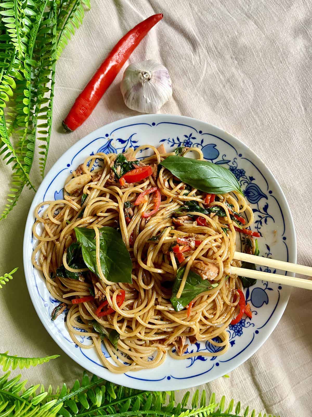 A plate of Thai Drunken Noodles Spaghetti next to chili and garlic.