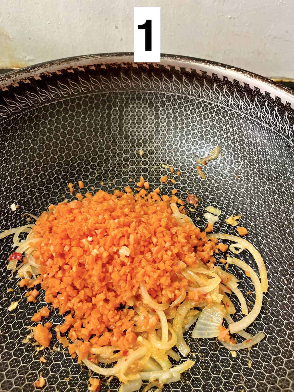 Stir-frying onions and diced carrots in a large wok.