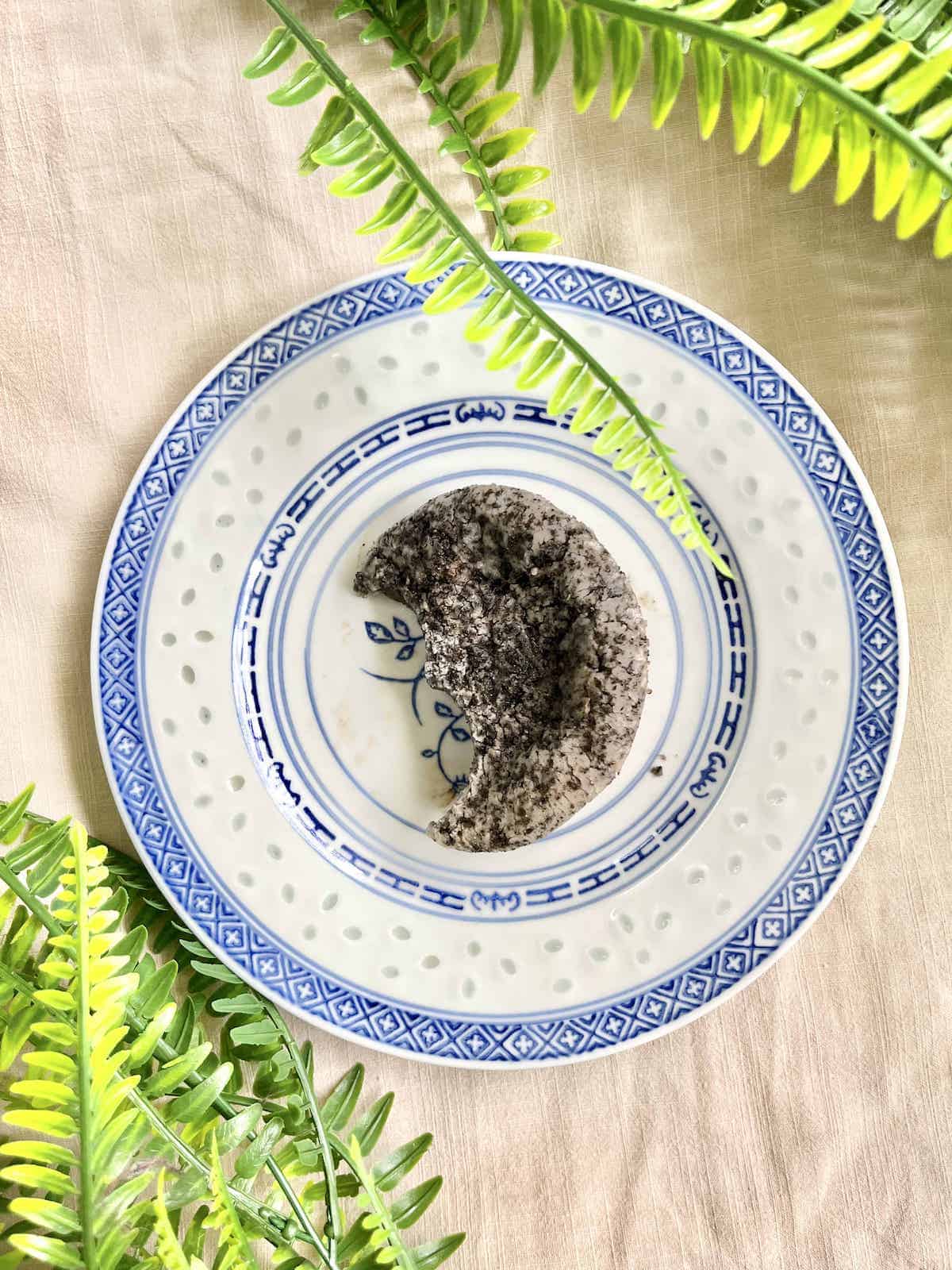 A half-eaten vegan black sesame mochi muffin on a Chinese plate.