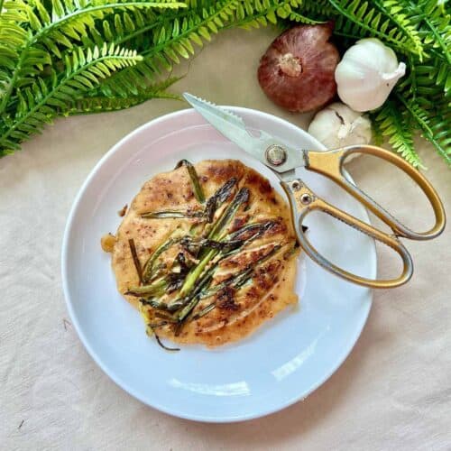 Homemade Korean scallion pancake next to a scissors.