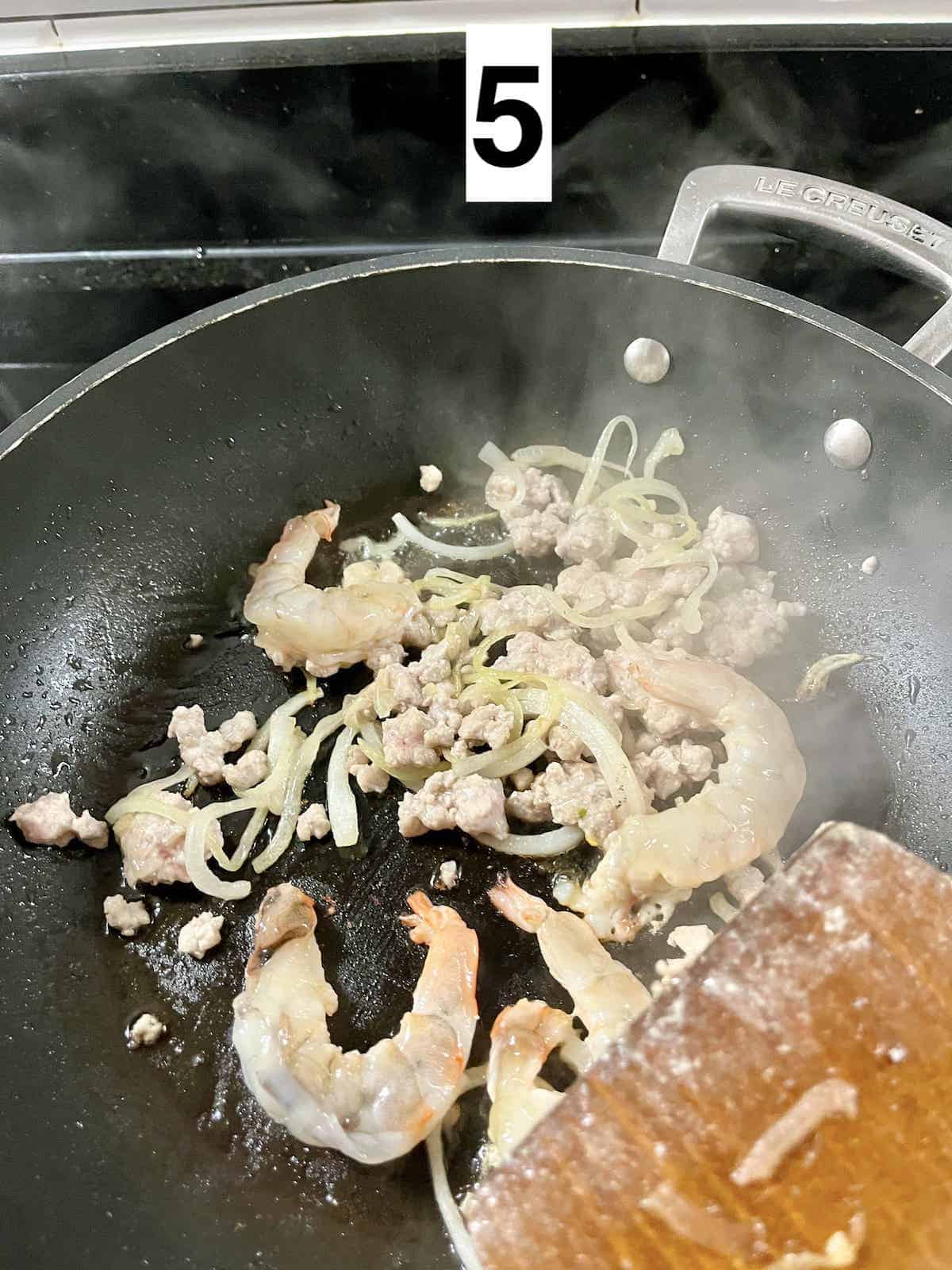 Stir-frying shrimp, pork and onions in a skillet.