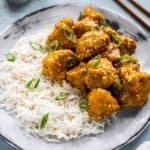 Cauliflower with sesame seeds next to rice and sliced green onions.