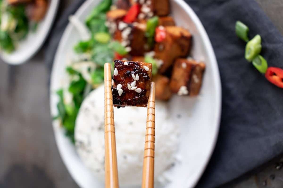Someone using chopsticks to pick up a pan fried tofu