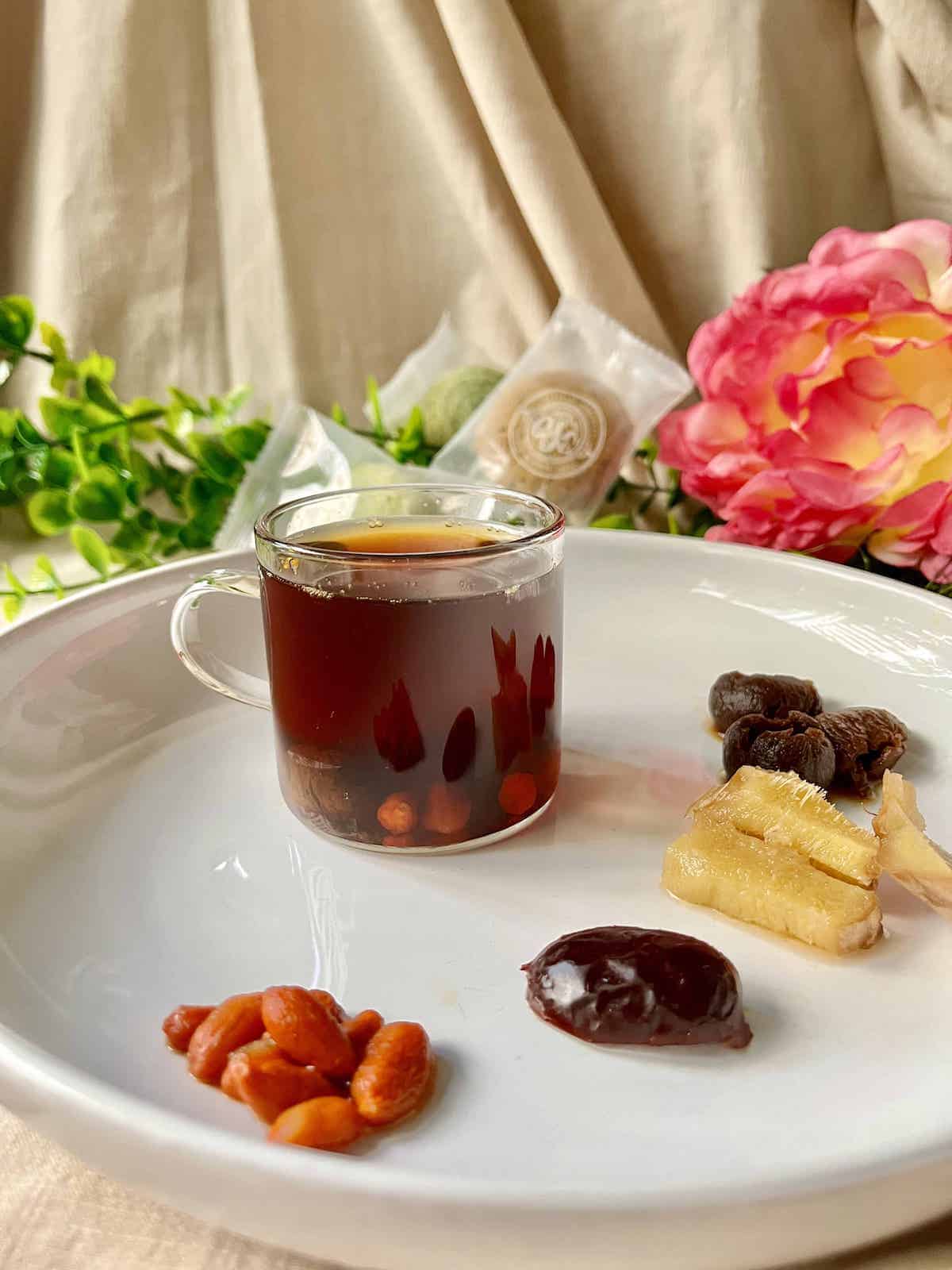 A cup of Chinese longan red date tea on a white plate with ingredients around it. 