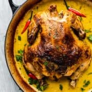 A nicely charred whole chicken in a yellow creamy sauce in a Dutch oven.