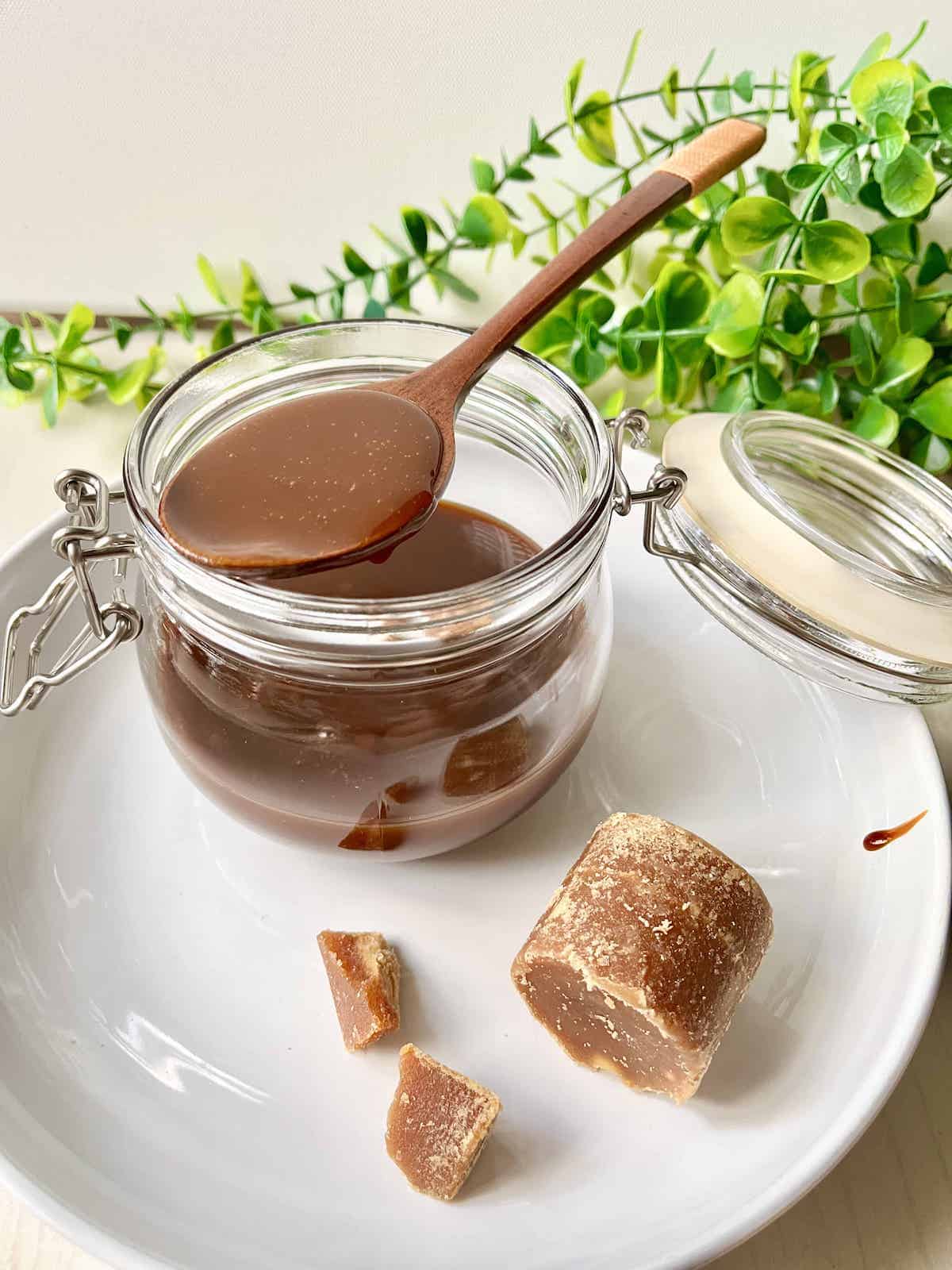 A jar of thick homemade plant-based coconut caramel with gula melaka sugar in front.