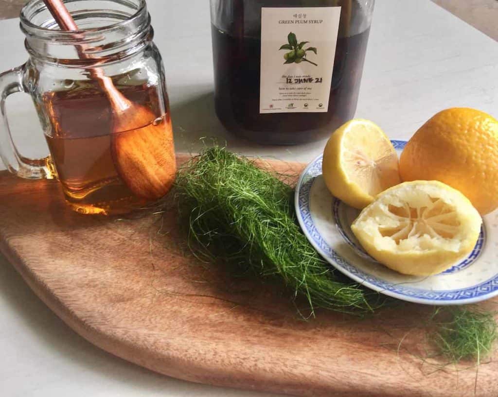 A cup of fruit tea made by stirring Korean plum syrup into hot water with lemons next to it