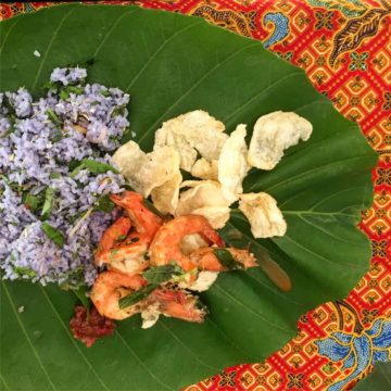 Nasi ulam, emping and butter prawns with curry leaves served on a banana leaf.