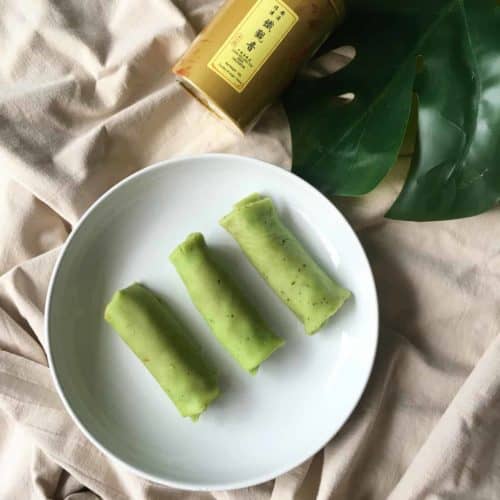 3 kueh dadar or pandan coconut rolls on a plate.