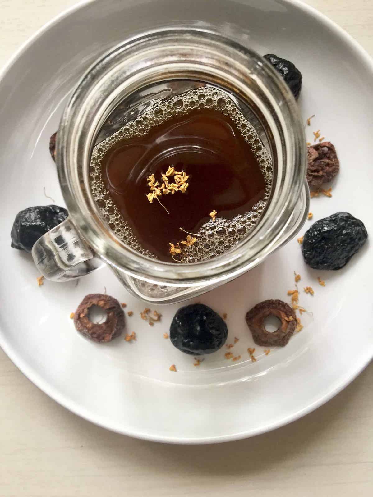 A cup of Chinese suanmei tang drink with preserved plums and hawthorns around it