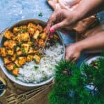 A hand picking up some paneer cubes that have been tossed in honey sriracha sauce