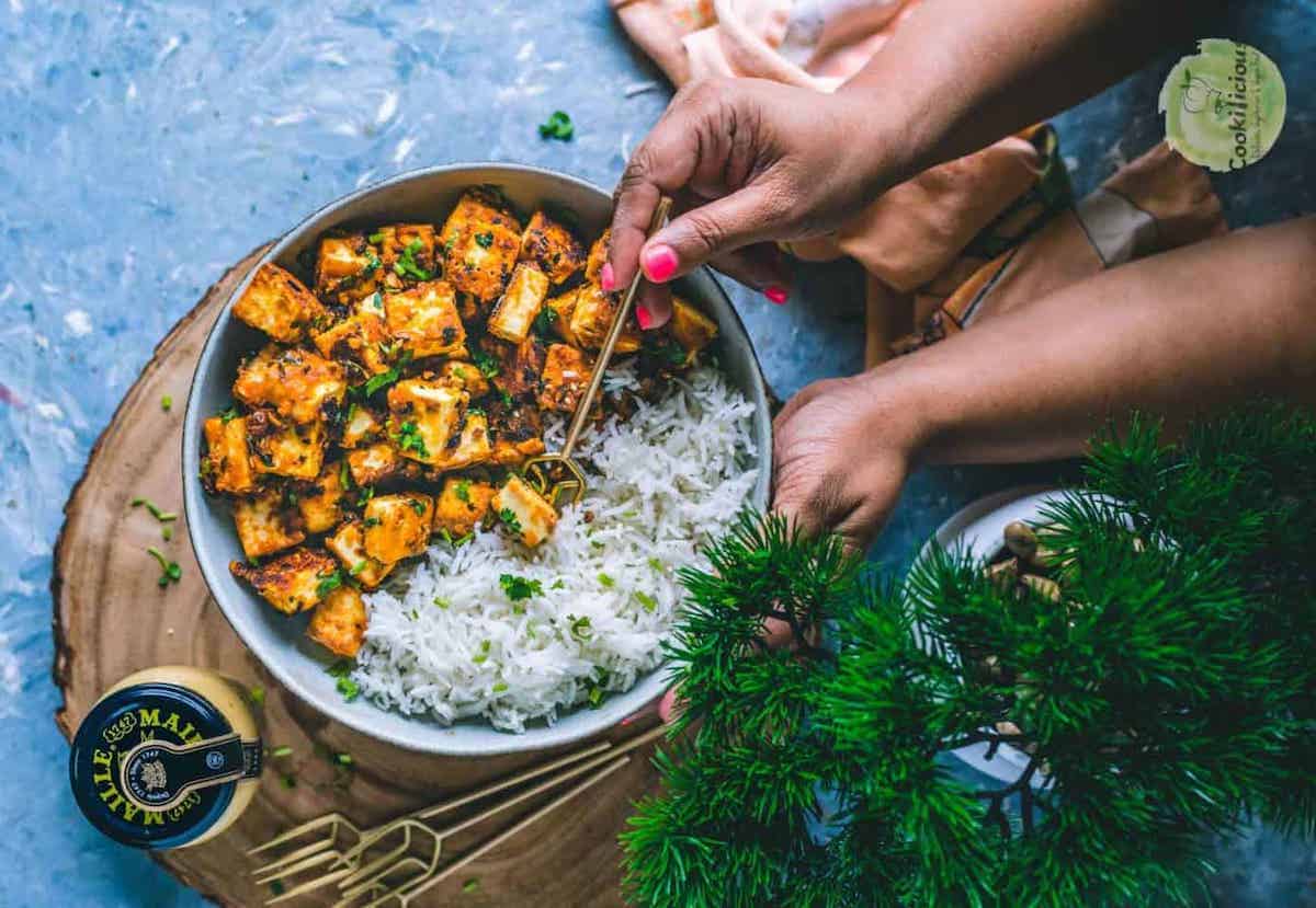 A hand picking up some paneer cubes that have been tossed in honey sriracha sauce