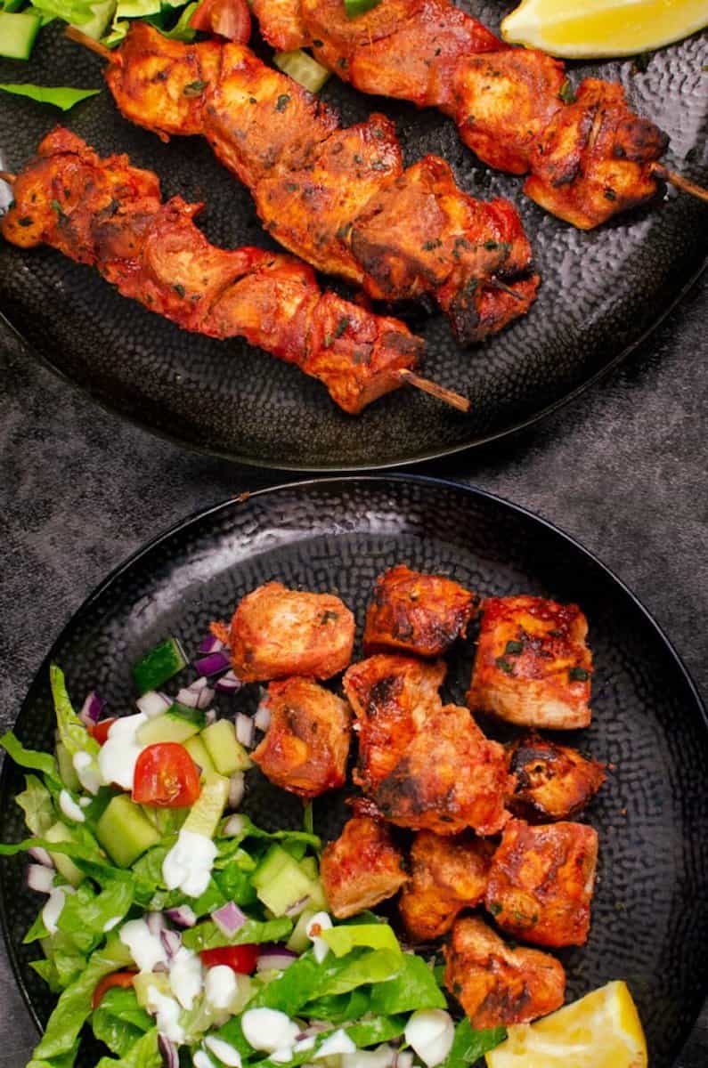 2 plates full of tandoori chicken, some of which are skewered on sticks.