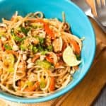 A bowl of stir-fried noodles tossed in a Thai peanut sauce in a blue bowl