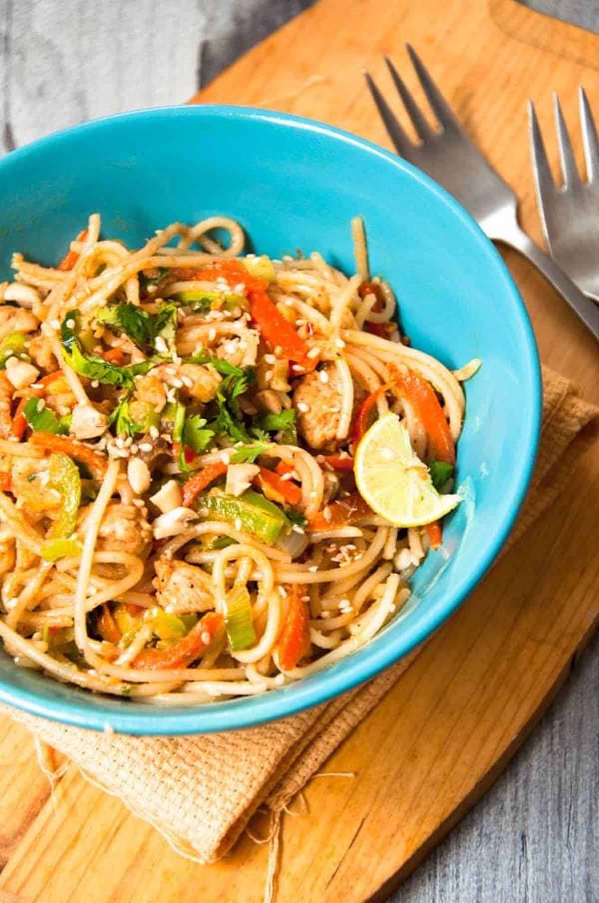 A bowl of stir-fried noodles tossed in a Thai peanut sauce in a blue bowl