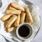 A basket of golden egg rolls with dipping sauce