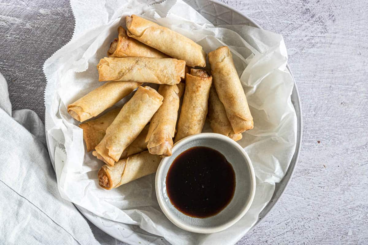 A basket of golden egg rolls with dipping sauce