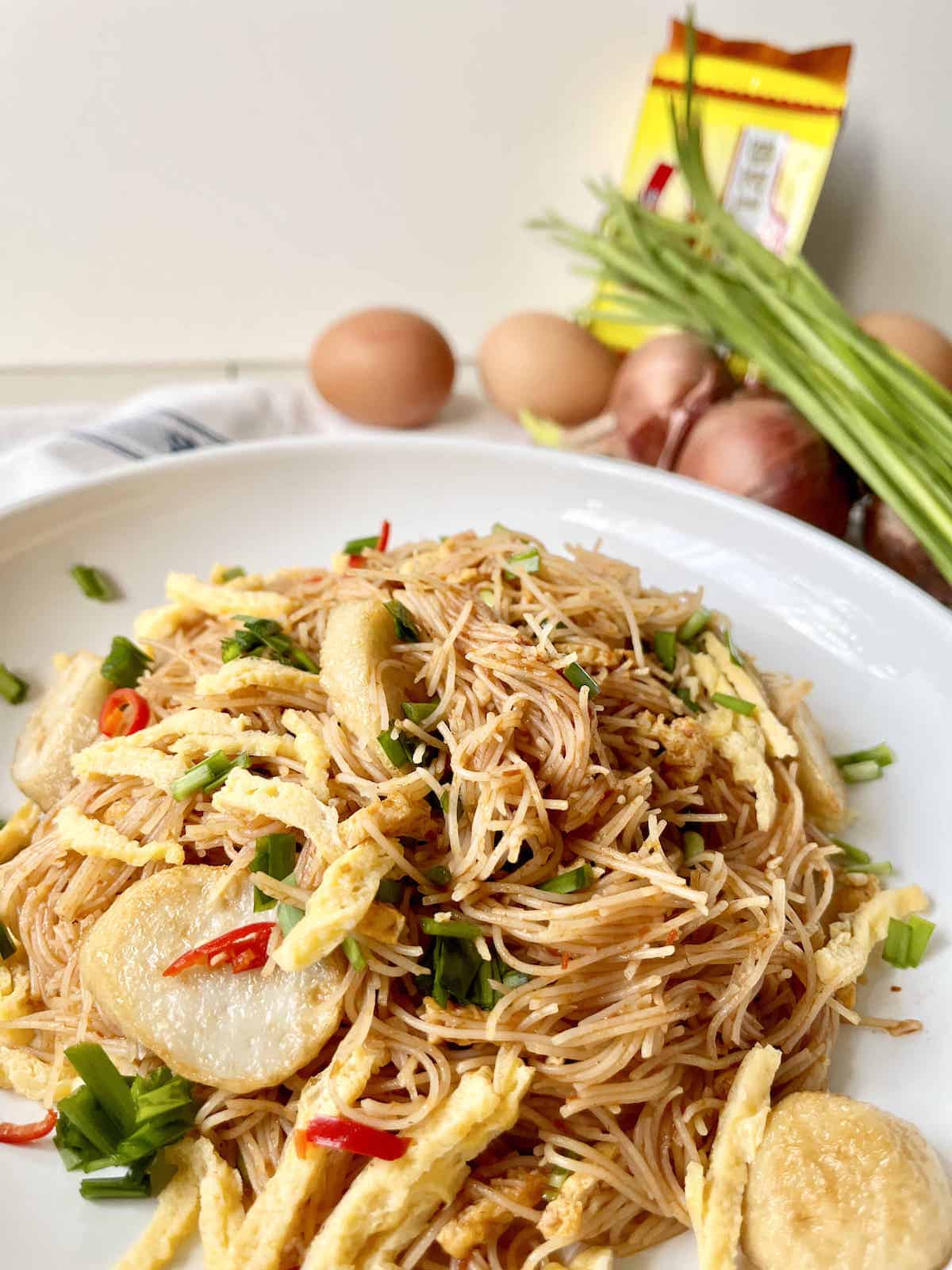 Stir-fried Singaporean Mee Siam with omelette and fishcakes on a white plate.