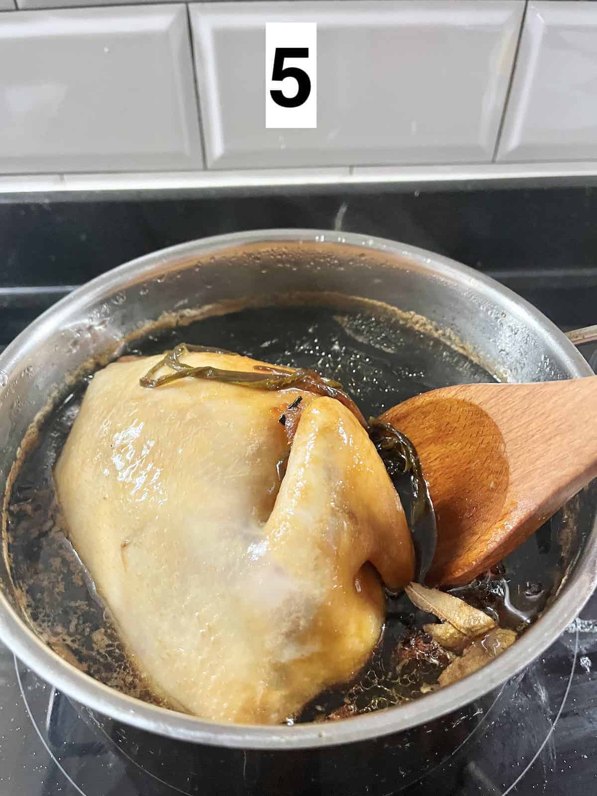 Using a wooden spatula to baste the whole chicken with hot soy sauce.