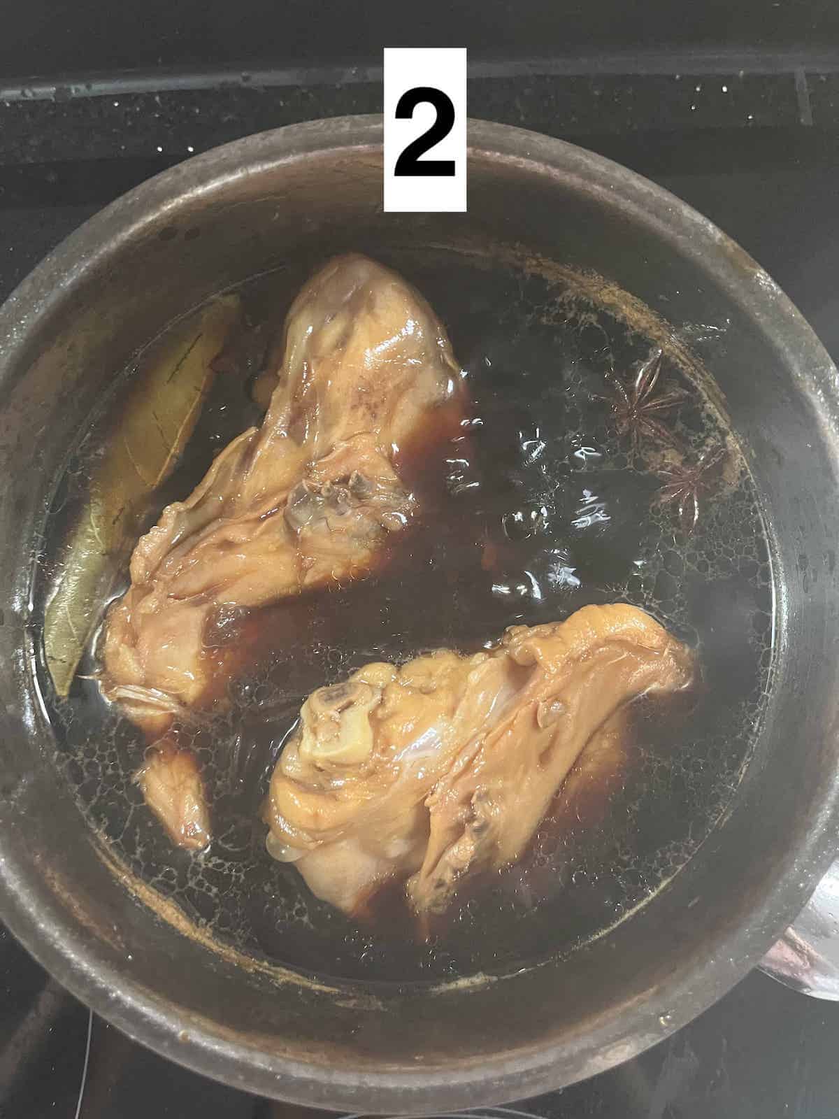 2 chicken thighs in soy sauce braising liquid with some bubbles around them.