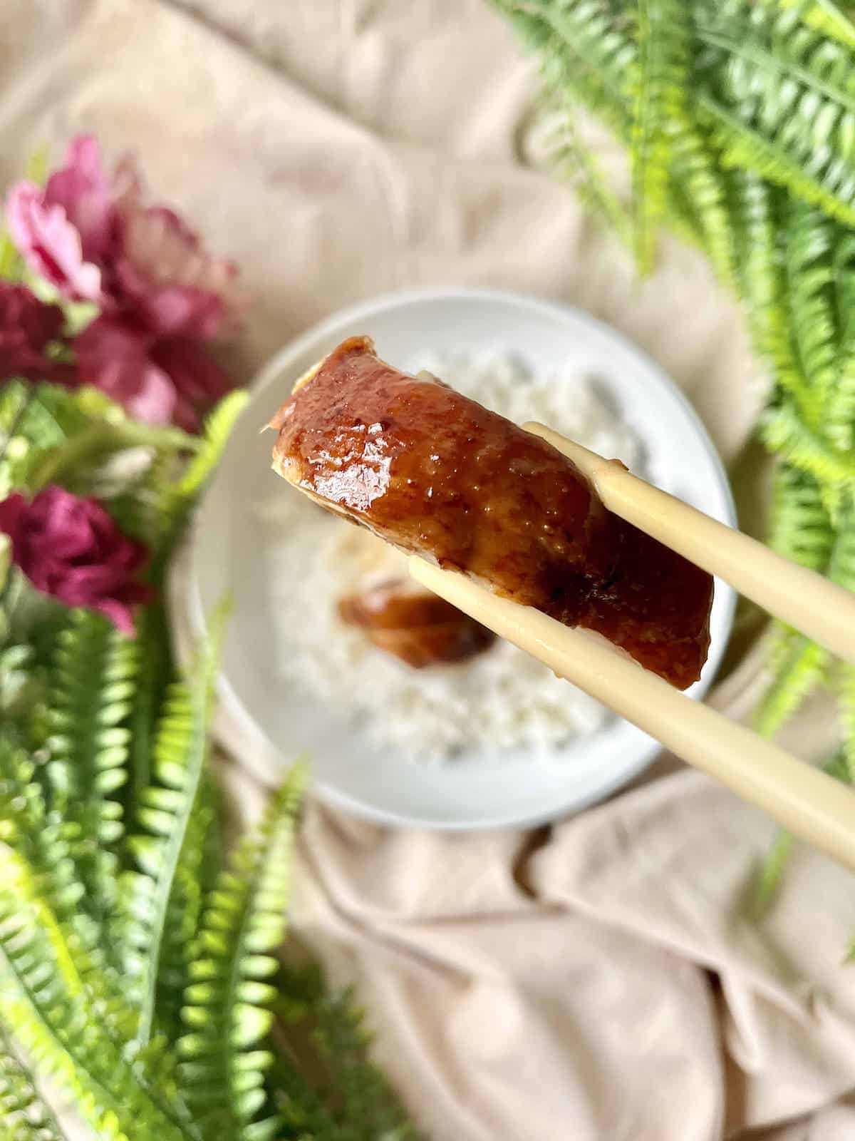 Using chopsticks to pick up a piece of soy cooked chicken thigh.