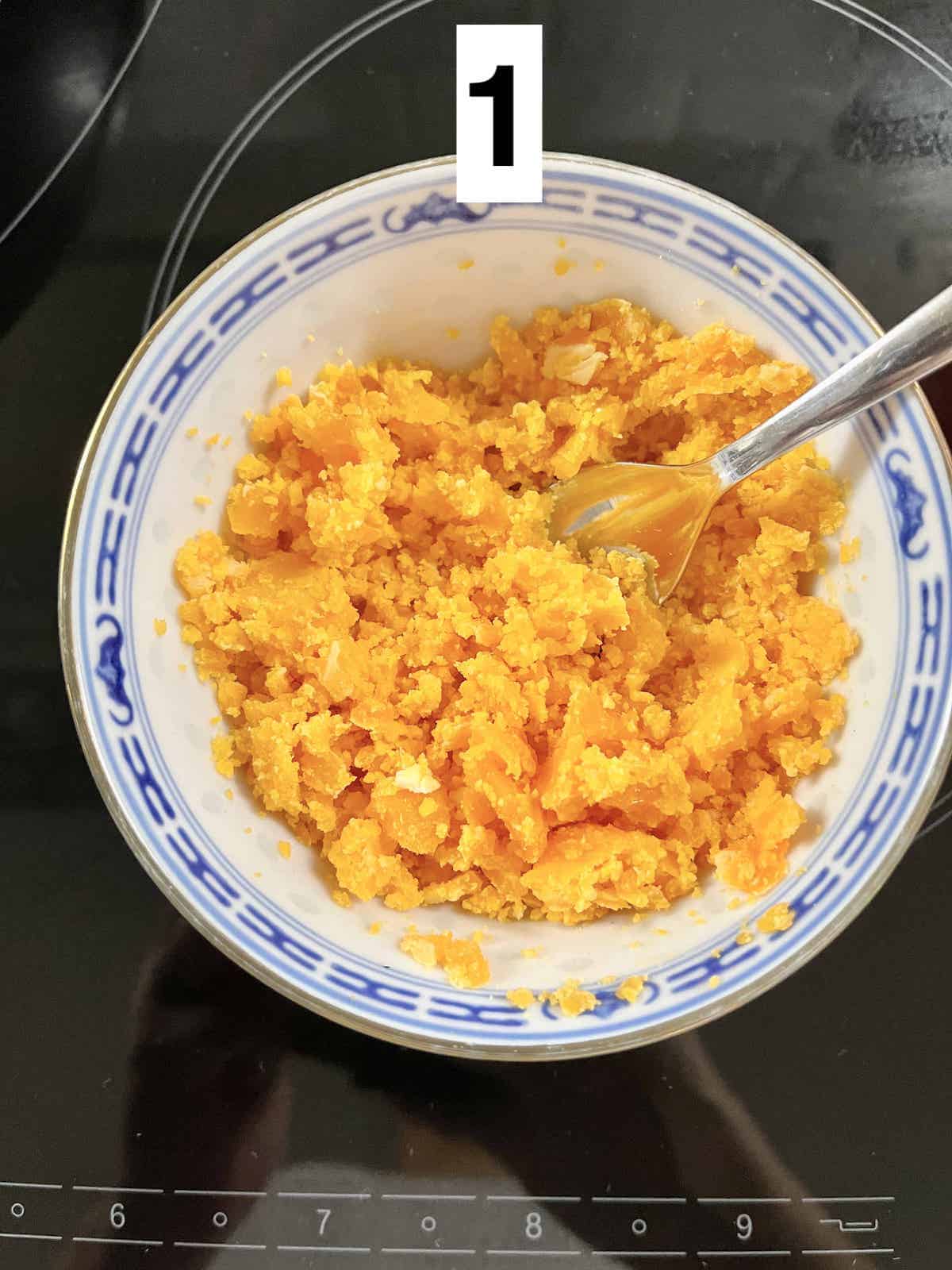 Mashing salted egg yolks in a bowl with a fork.