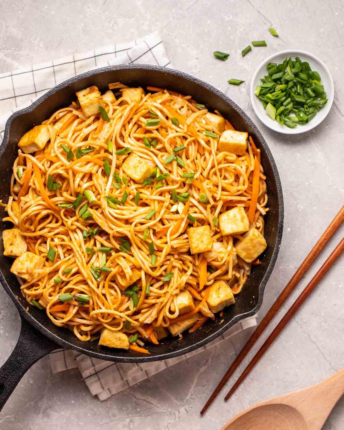 A skillet brimming over with noodles cooked in a peanut sauce and tofu