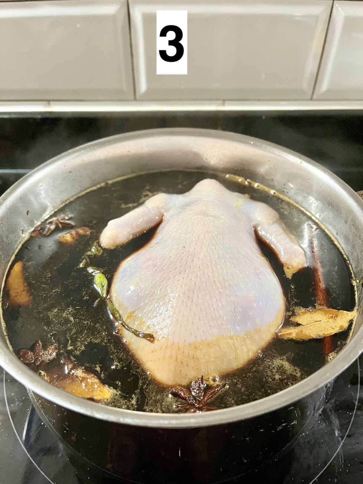 A whole chicken poaching in a pot of soy sauce braising liquid.