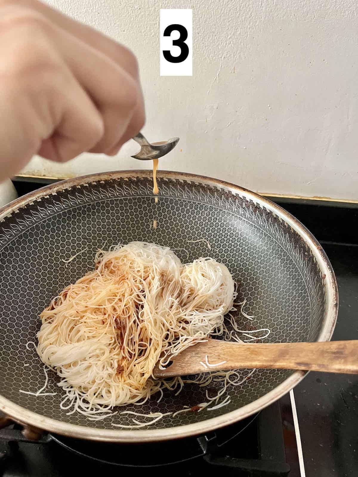 Adding tamarind juice and seasoning to a wok of bihun noodles.