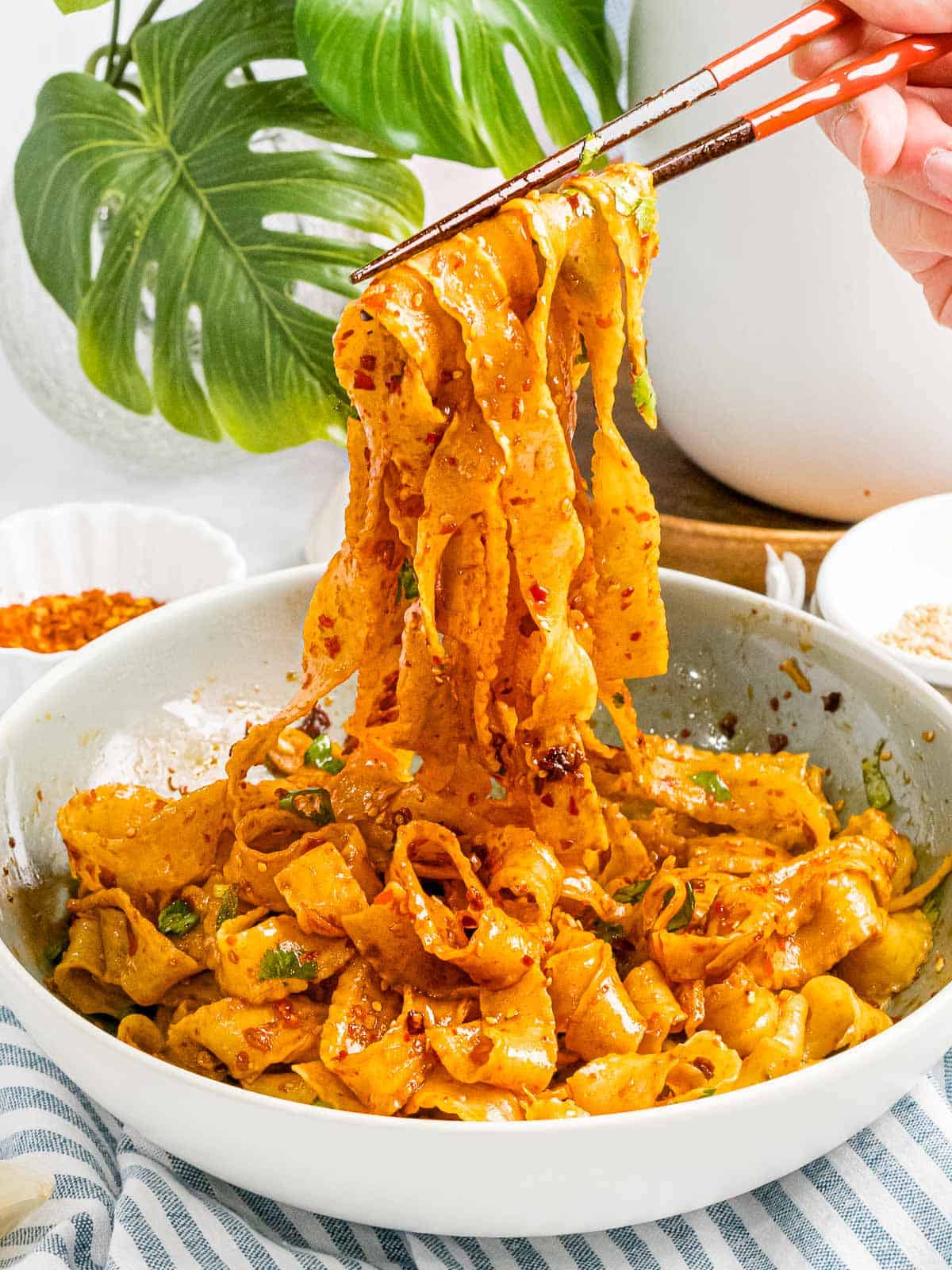 A pair of chopsticks lifting some red sichuan chilli noodles out of a plate