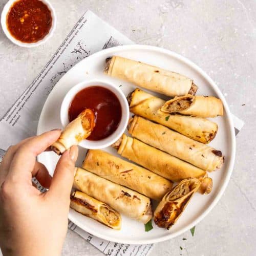 A hand dipping a vegan lumpia into sauce